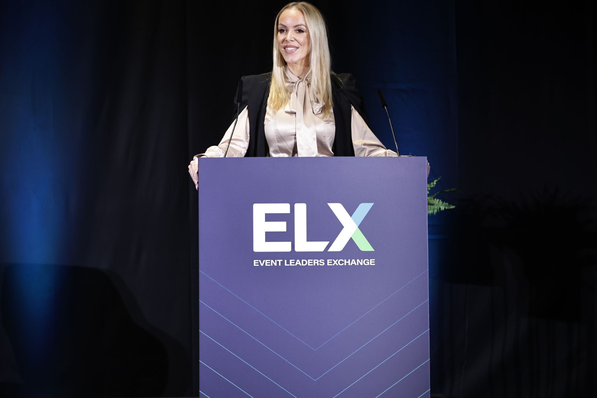 Chloe emceeing from the podium at Event Leaders Exchange